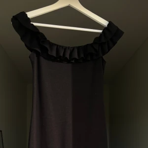 Svart klänning med volang  - Svart off shoulder klänning med volanger. Klänningen är i midilängd. Använd en gång så jättebra skick. 