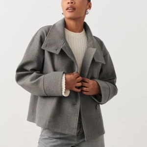 Vårjacka Gina Tricot - Kort kappa med hög krage. Kappan är grå och har oversize fit. Den har knäppning fram, raka ärmar och breda slag.