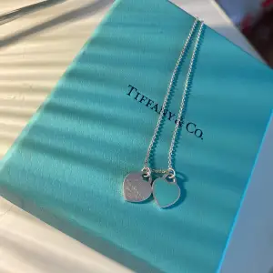 Ett tifanny and co halsband med två hjärta där ett är blått och det andra är grått med deras märke, Använt typ 7 gånger men endå i fint skick. Boxen ingår men har tycärr inte kvittot. Skriv vid intresse!💕