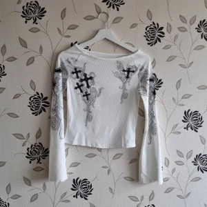 Vit något croppad långärmad topp, Strl: S, Y2K - Vit långärmad topp med kors i Y2K-stil. Vida ärmad och ribbad modell. Nyskick! OBS! Jag kan inte skicka något vecka 26.
