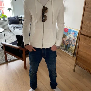 Vit Zip-Up Hoodie - Tja! Säljer denna feta zip-up tröjan som är i nyskick. Modellen är ca 171cm. Skriv gärna för fler frågor eller funderingar!