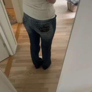 Lågmidjade bootcut jeans  - Säljer dessa ikonisk jeans med kronor på  eftersom de inte passar mig längre, knappen är av men brukar lösa det genom att trä en hårsnodd där den ska vara. Annars är de i bra skick!