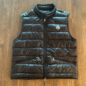 Moncler Gui - Säljer nu min svarta Moncler gui väst som passar perfekt till våren och sommaren! Västen är i storlek 2 och är lite för liten för mig. Skicket är 7/10 då den har 2 jätte små hål. Har även äkthetsbevis, hör av er vid frågor!