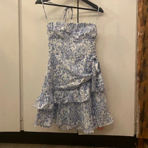 Blommig klänning - Helt ny supersnygg klänning i bra kvalitet. Den har volanger och en rosett, perfekt till utomlandsresan🤍💙 Enbart testad, beställde hem och den är alldeles för liten. Lapp sitter kvar. Rekommenderar för de med lite mindre byst. 