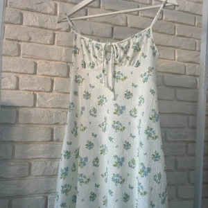 KLÄNNING - En söt klänning från Gina tricot i jättebra skick. Klänningen är vit med blåa blommor och gröna blad. Klänningen är i strl XXS men sitter dock bra som XS och S.