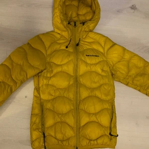 Peak Performance Helium dunjacka *Nyskick* - Superfin dunjacka från Peak Performance som endast använts ett fåtal gånger, nyskick utan skador, revor eller skavanker. Senapsgul, strl XS. Nypris: 2200:-