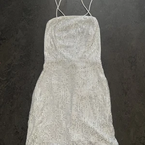 Paljettklänning XS - Paljettklänning, lårkort, tight modell, tunna band med korsat i ryggen.  Storlek: XS/34 Färg: Silver, med vitt undertyg.   Endast provad!! Samfraktar gärna 