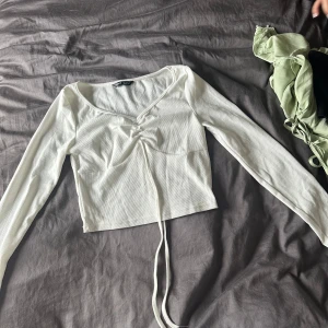 Vit långärmad topp - En vit långärmad topp med en v-ringad hals och snörning framtill. Toppen är croppad och har en åtsittande passform.