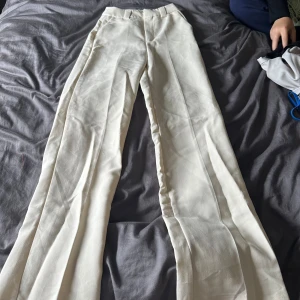 Vita byxor - Ett par beiga kostymbyxor med hög midja och raka ben. Byxorna har en klassisk design och två bakfickor.