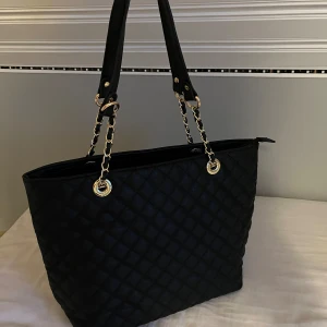 ”Ribbad” handväska  - En ”ribbad” handväska med ett stort fack med dragkedja, tre små fack i varav ett har dragkedja, ett litet dragkedje-fack på baksidan. En rymlig väska perfekt till skolan. 