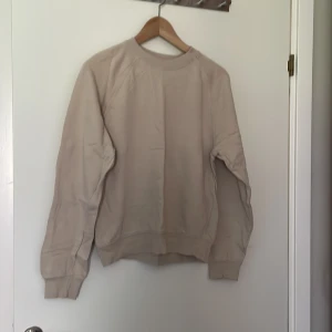 Beige tröja från C - En beige tröja från Cubus tillverkad av ekologisk bomull. Tröjan har långa ärmar och ribbstickade muddar vid ärmslut och nederkant.