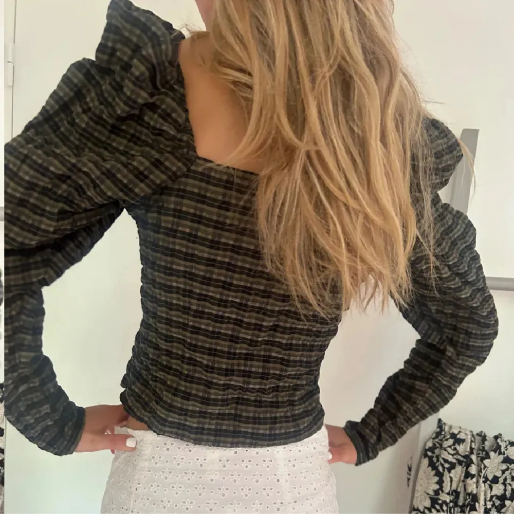 En rutig långärmad topp med fyrkantig halsringning och puffärmar. Toppen har en tight passform och är i mörka färger med inslag av grönt och svart. från hm lånade bilder. inga defekter alls aldrig använd. Yläosat.