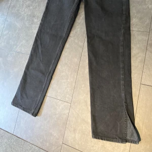 Svarta Jeans med slits - Svarta jeans från Gina Tricot, stl 36. Beninnerlängd 77 cm. Längst ner på jeansen finns en slits på ”yttersidan” av benet. Fint skick, mycket sparsamt använda.