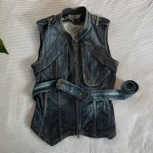 Jeansväst - Mörkblå jeansväst med dragkedja. Väldigt bra skick och fin kvalitet. Ett midjeband tillkommer men går också att ta av. Om du har fler frågor eller önskar ytterligare bilder är det bara att skriva!