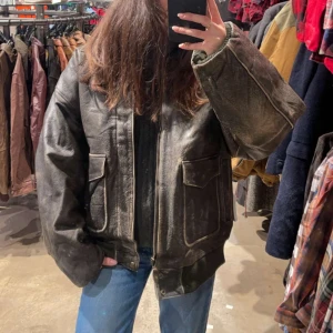 Vintage skinnjacka - En snygg och klassisk skinnjacka med en avslappnad passform. Jackan har två fickor framtill och en dragkedja framtill. Den har en snygg vintage-look och är perfekt för att addera en touch av stil till din garderob. Köpt för 1 299kr