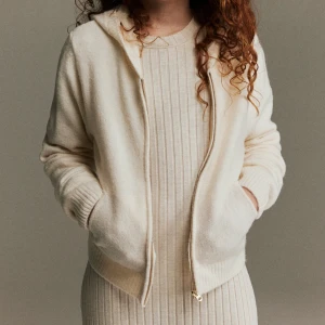 Beige stickad jacka med dragkedja - En beige stickad jacka med dragkedja framtill. Jackan har långa ärmar och en huva. Den är tillverkad i ett mjukt och bekvämt material.Supersnygg stickad munkjacka som är superbra !! Den är i bra skick men är nopprig och är lite lite smutsig på nopprarna, annars i superbra skick ❣️