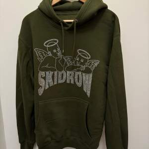 En mörkgrön skidrow hoodie med mönster gjort av paljetter.