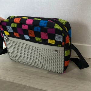 Väska  - Super cool färg rutig ny axelväska som man kan designa själv med små bitar man knäpper på den gråa plattan för att göra en bild.⭐️ Insidan har mycket utrymme och fack tex dator osv. Passar även som skolväska! Mått:   36 cm bredd  26 cm hög 6 cm tjock