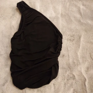 Topp, axellös - Glittrig svart topp. En axel "axellös"