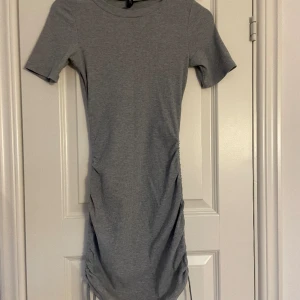 Tajt klänning  - Grå tajt klänning från H&M i storlek xss, den är skrynklig på sidorna med band. Bra skick använd några gånger.