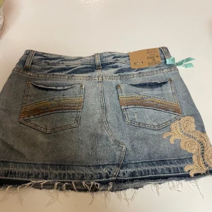 Jeanskjol - Jeanskjol med snygga detaljer. Guldiga detaljer fram och baktill samt ett band bak. Storlek 5/6 passar bra för S. 