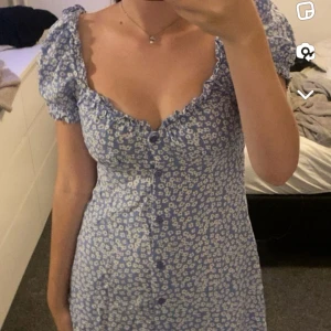 klänning - Klänning som är använd 1 gång, ljusblå med vita blommor och lila/blå knappar 