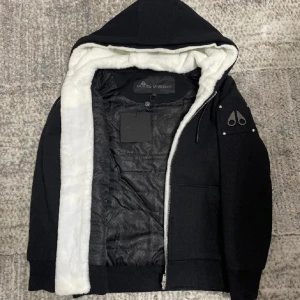 Moose knuckels -  Säljer denna helt nya omtyckta moose knuckles hoodie/jackan i färgen svart och vit päls inne i hoodie/jacka. Man kan även ta bort den vita pälsen där inne. NFC Scan finns för att verifiera att den är äkta. Vid funderingar är det bara att höra av sig