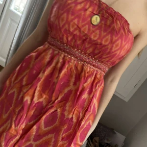 Söt mönstrad sommarklänning! - Jättefin mönstrad sommarklänning som är orange - röd mönstrad, med fina paljetter och axelbandslös! Aldrig använd men köpt second hand!
