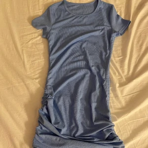 Klänning  - Ljusblå klänning. Aldrig använd, man kan göra den både hel lång och kort bara att justera med snörningen som sitter på sidan 