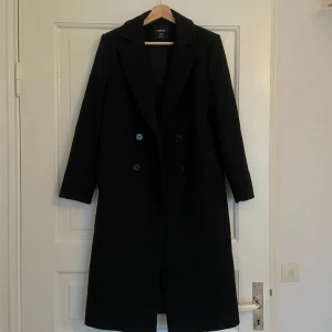 Kappa i ull NYSKICK - Svart kappa från Lindex i ullblandning.  Dubbelknäppning med slits bak.  Helt ny, aldrig använd! Säljer då den tyvärr inte kommit till användning. Nypris 1499kr.