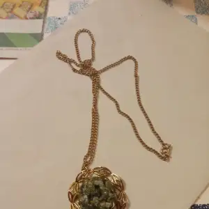 Vackert halsband med hänge av en blomma och gröna stenar i mitten guldfärgad ,inget slitage finnes .
