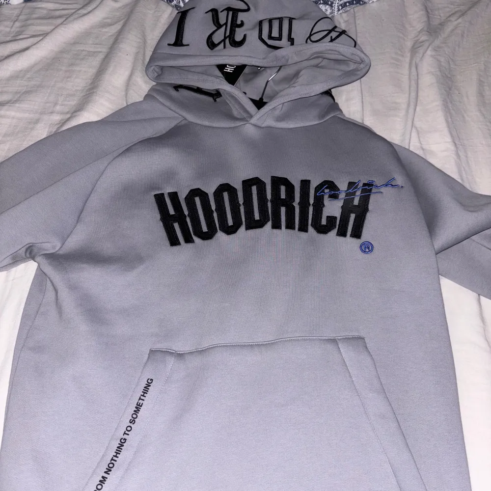 Säljer en snygg grå hoodie från Hoodrich. Den är i nyskick och har en stor ficka på magen samt texten 'HOODRICH' tryckt över bröstet. Perfekt för höst och vinter, och den är superbekväm att ha på sig. Passar bra till både vardag och chill.. Tröjor & Koftor.