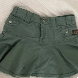 Grön kjol från Bench - Säljer en snygg grön kjol från Bench. Kjolen har en normal passform och är tillverkad i bomull. Den har praktiska fickor med knappar och en dragkedja framtill. Perfekt för vår och sommar! Jag köpte den förut här på plick men den passa tyvärr inte❤️Jag köpte den för 450, men säljer för 300 då jag inte har lika stort plick konto än❤️❤️