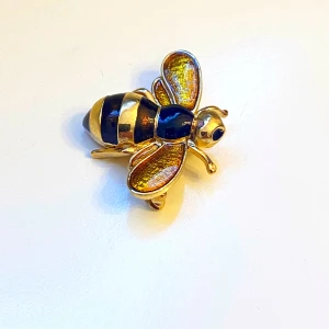 Guldfärgad bi-brosch - Säljer en superfin guldfärgad brosch i form av ett bi. Broschen har detaljer i svart och guld, med skimrande vingar som ger en extra touch. Perfekt accessoar för att piffa upp vilken outfit som helst! 🐝✨