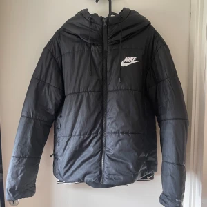 Svart pufferjacka från Nike - Säljer en svart pufferjacka från Nike. Jackan har en dragkedja framtill och en huva med dragsko. Den är perfekt för kalla dagar och har en sportig stil. Jackan är i bra skick och redo för en ny ägare. Passar perfekt till vintern men även höst.