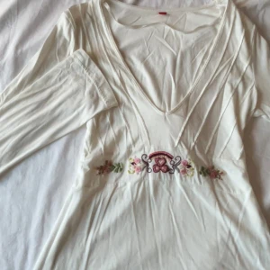 Långärmad tröja med broderier  - Långärmad vit tröja med broderier, knytbar där bak. Tröjan är i gott skick med endast en liten missfärgning på ena tröjärmen (se sista bild). Gjord på 60% bomull och 40% modal. Storlek L, men har en liten passform, så funkar även på en stl: S/M
