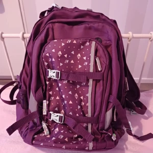 Lila ryggsäck med mönster - Säljer en snygg lila ryggsäck med geometriskt mönster. Ryggsäcken har flera fack och justerbara remmar för bästa passform. Perfekt för skolan eller utflykter. Den har också reflexdetaljer för ökad synlighet i mörker. Väldigt praktisk och rymlig och speciell fack för hörlurar!!