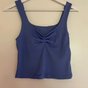 Blå ärmlös linnetopp - Säljer en snygg blå ärmlös linnetopp. Toppen har en enkel design med en liten rynkdetalj framtill. Perfekt för sommardagar eller som ett lager under en jacka. Den är bekväm och lätt att matcha med olika outfits.