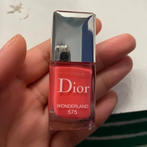 Rött nagellack från Dior - Säljer ett superfint rosa nagellack från Dior i färgen Wonderland 575. Det kommer i en elegant glasflaska med en silverfärgad kork. Perfekt för att ge dina naglar en lyxig touch!