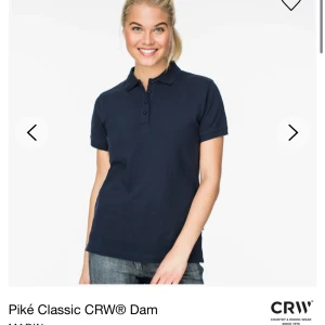Mörkblå pikétröja från CRW - Säljer en mörkblå pikétröja från CRW i storlek S. Tröjan har korta ärmar och en klassisk krage med knappar framtill. Materialet känns mjukt och bekvämt mot huden.