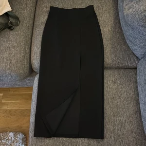 Svart lång kjol från Gina i storlek XS - Kjolen har en sluta. Stretchigt material Den är knappt använd.