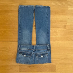 Blå bootcut jeans från Gina Tricot - Säljer ett par snygga blå bootcut jeans från Gina Tricot. De är i storlek 146 med knappar och dragkedja. Perfekta för en avslappnad men ändå stilren look. Passar bra till både vardag och fest!
