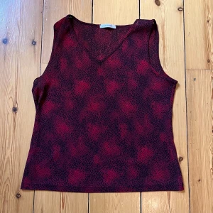 Röd och svart ärmlös topp - En röd och svart ärmlös topp med ett unikt mönster. Toppen har en v-ringad hals. Ingen storlek men väldigt stretchig, så passar L-XL. väldigt smickrande fit ❤️‍🔥inga bilder på! 