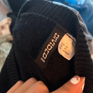 Svart stickad tröja från Divided - Säljer en svart stickad tröja från Divided i storlek XS. Tröjan är perfekt för höst och vinter med sin mysiga och varma känsla. Den har en normal passform och är långärmad. Perfekt att matcha med jeans eller kjol för en snygg och bekväm look.