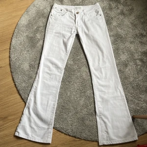 Vita bootcut jeans  - Säljer ett par snygga vita bootcut jeans. De är i storlek XS/S och har en klassisk femficksdesign med en snygg broderad detalj på bakfickan. Jeansen är tillverkade i bomull och har en knapp och dragkedja framtill. Perfekta för både vardag och fest! obs de har en liten fläck på framsidan (se bild 2) men det går förmodligen bort i tvätten!