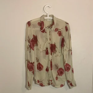 Blommig blus från nygårdsanna  - Fin blus som är ite genomskinligt vit med röda rosor på från nygårdsanna. Storlek large. Använd men bra skick.