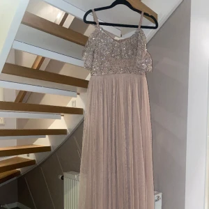 Lång klänning  - En fin nude lång klänning med paljetter på. Ärmarna hänger ned för axlarna. Klänningen är i god skick och använd endast en gång. Den är köpt från Zalando.