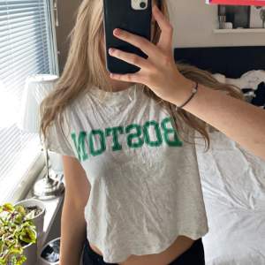 Grå liten t-shirt med ett grönt text tryck . Har en liten fläck på baksidan av tröjan