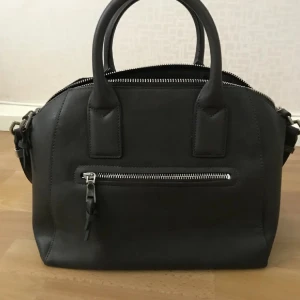 Svart handväska👜 - En elegant svart handväska från märket Mango med dragkedja framtill. Knappt använd och är som i nyskick. Axelband medföljer👜