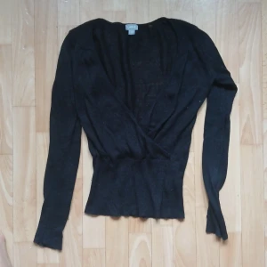 Svart omlott-tröja från Lindex - En svart omlott-tröja från Lindex med lång ärm och ribbad nederkant. Tröjan har en djup v-ringning och är tillverkad i ett stickat material.